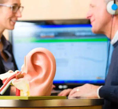 Patient undergoing a hearing evaluation with an ear model in the foreground